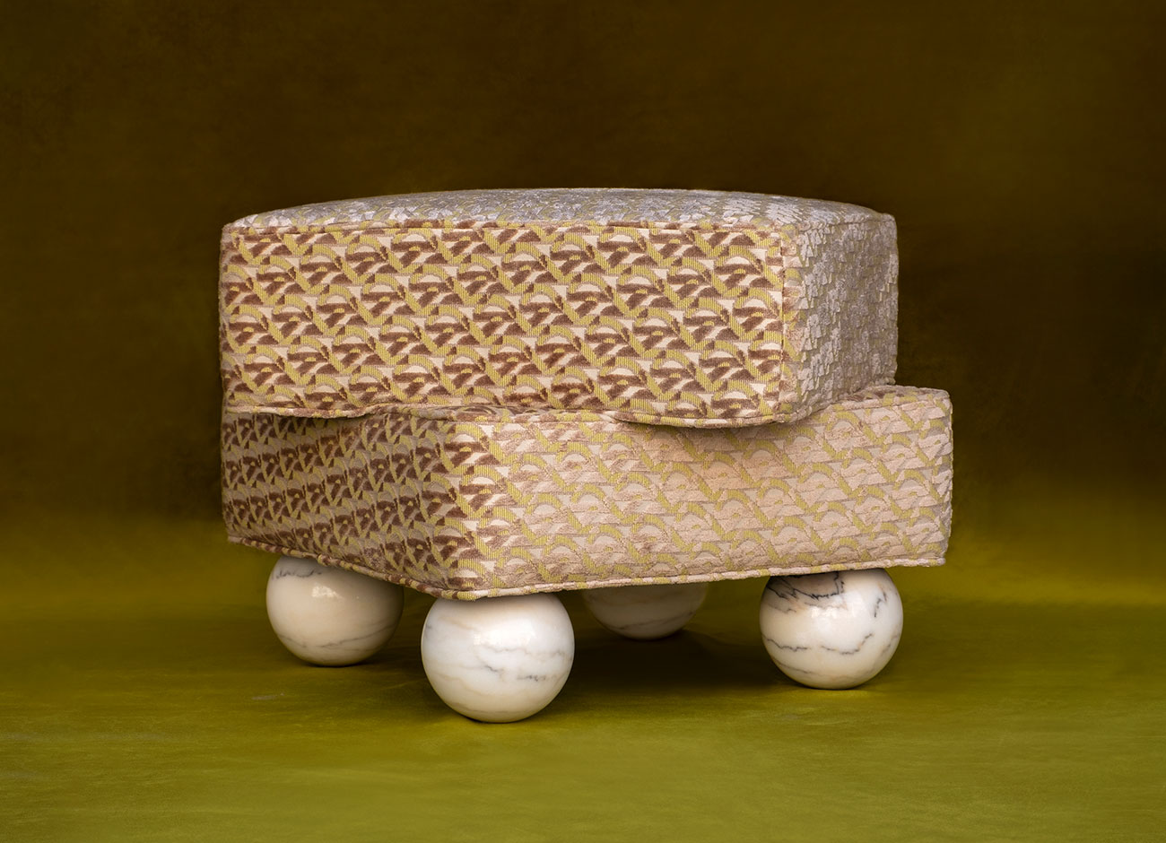 Madonna stool Madonna stool upholstered in a patterned fabric by kirkby design monogram zest k5303/03 with marble sphere legs, set against a green background.