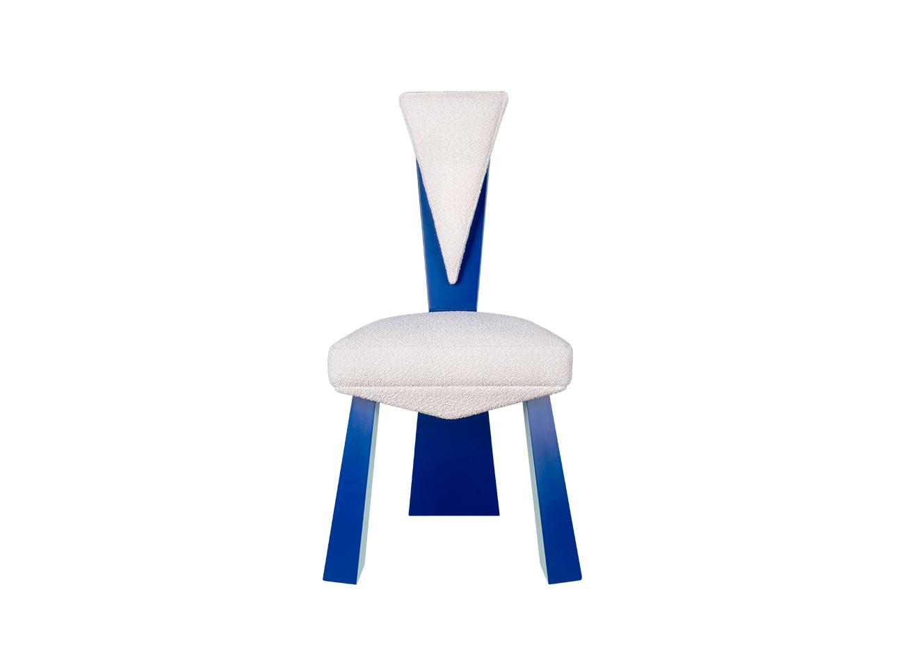 Kju bist dining chair by malabar, front-facing against a white background, highlighting its cubist-inspired angular structure, planar silhouette, blue lacquered legs, and bouclé fabric upholstery.