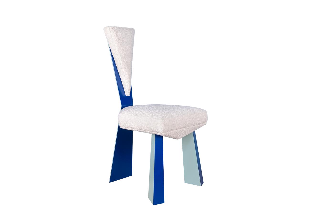 Kju bist dining chair by malabar photographed at a 45-degree front angle against a white background, emphasizing its cubist-inspired angular geometry, planar silhouette, blue lacquered legs, and bouclé fabric upholstery.