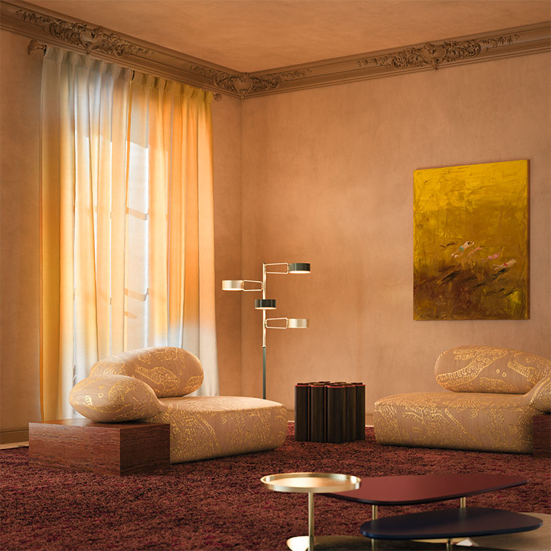 The Art of Bold Living: Viv Id Reimagined 1 Viv Id Reimagined chaise longue in a warm-toned living room interior, featuring Tiger Silk 002 fabric by Dedar with yellow highlights and a Travertino Rosso structure. The space also includes the La Toile center table, Kensington Tic-Tac-Toe table, and Brompton Floor Lamp.