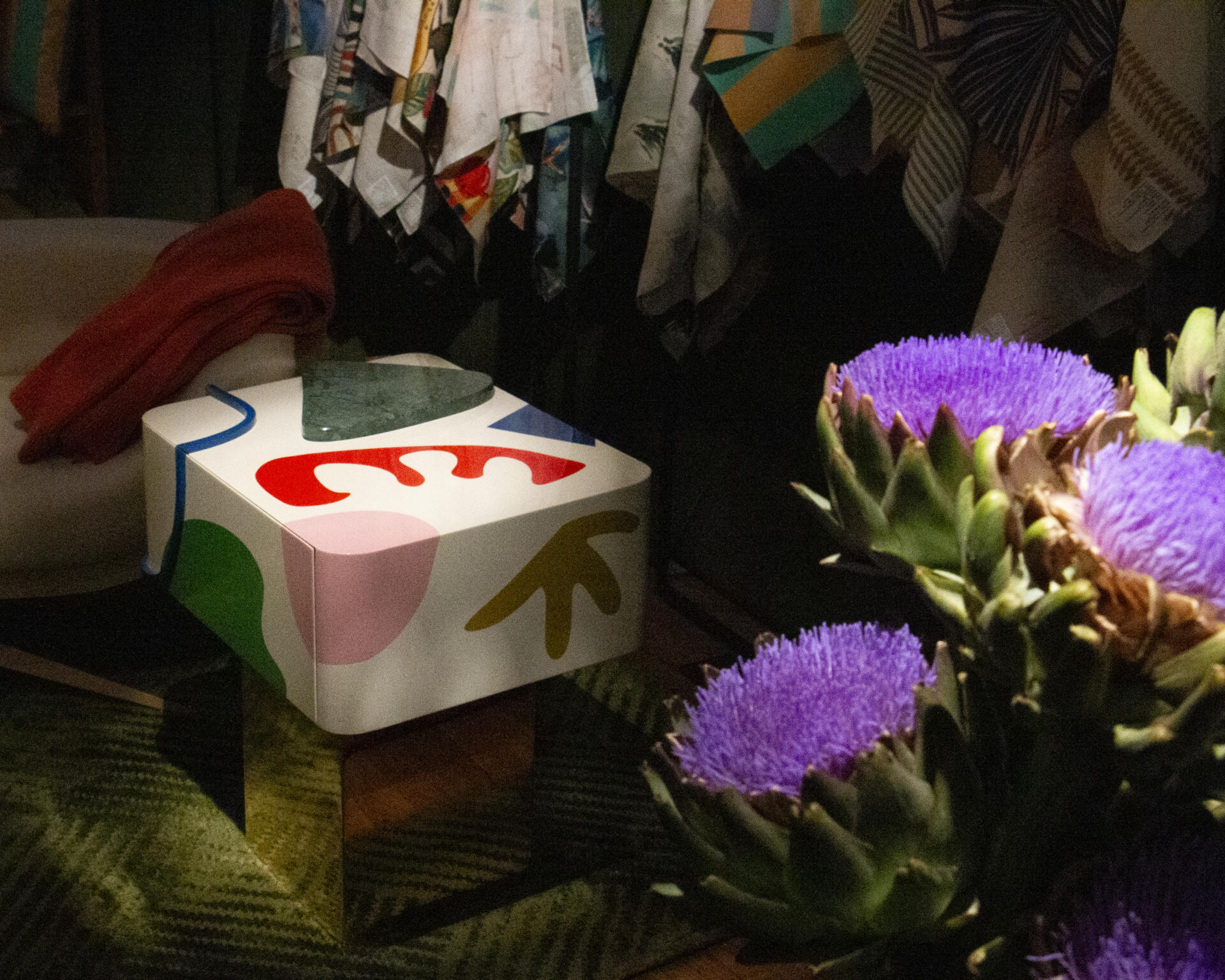Fauved bedside table at paris design week, illuminated with dramatic light and placed next to an arrangement of purple flowers.