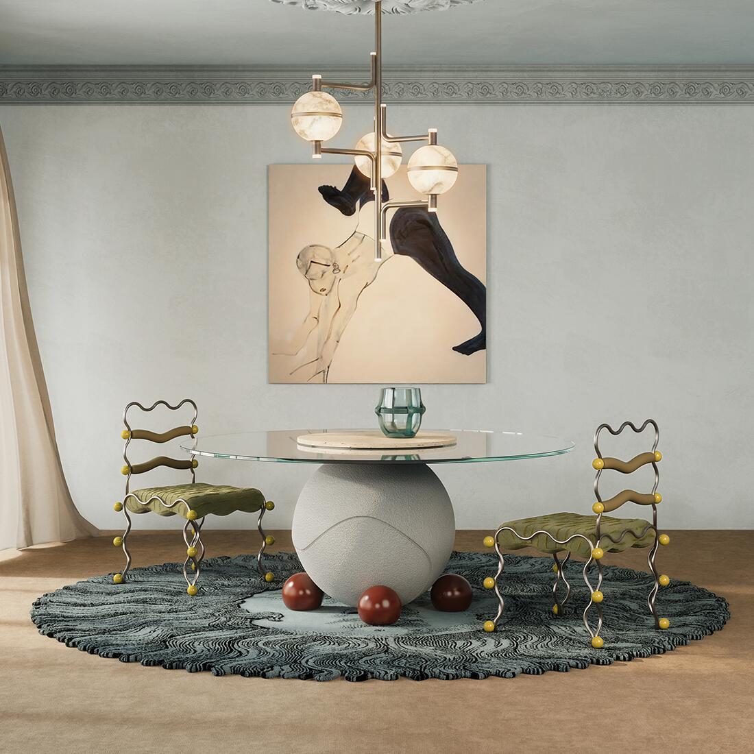 A contemporary dining room featuring a pair of Vela Dining Chairs by Malabar with wavy metal frames, olive green seats, and yellow spherical accents, arranged around the Circulus dinign table with a glass-top round and a spherical stone base. The room includes a textured blue circular rug, and the modern multi-globe Andros Suspension Lamp, and an abstract figurative painting on a light blue colored wall.