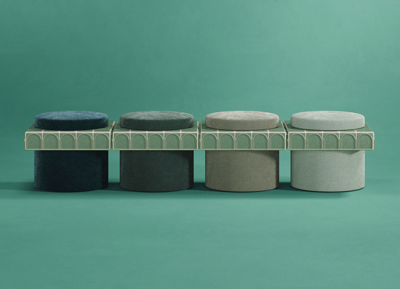 Enigma i stool A side-view photograph of four round stools arranged in a horizontal line, presenting a gradient of color. Each stool has a cylindrical fabric base and a matching round velvet seat, with a central square collar made of green ceramic tiles (barro. - emerald) featuring a repetitive arch pattern. The velvet fabric colors transition from deep blue on the left, to deep forest green, then olive green, and finally a light sage green on the right, all variations within the soft jade range. They are lined up against a seamless teal-green background, resting on a surface of the same color.